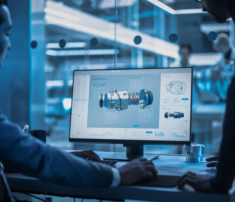 Engineers reviewing a 3D CAD model of a turbine component on a computer screen in a modern high-tech office.