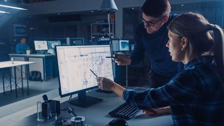 Engineers collaborating on technical blueprints displayed on a computer screen in a modern design office.