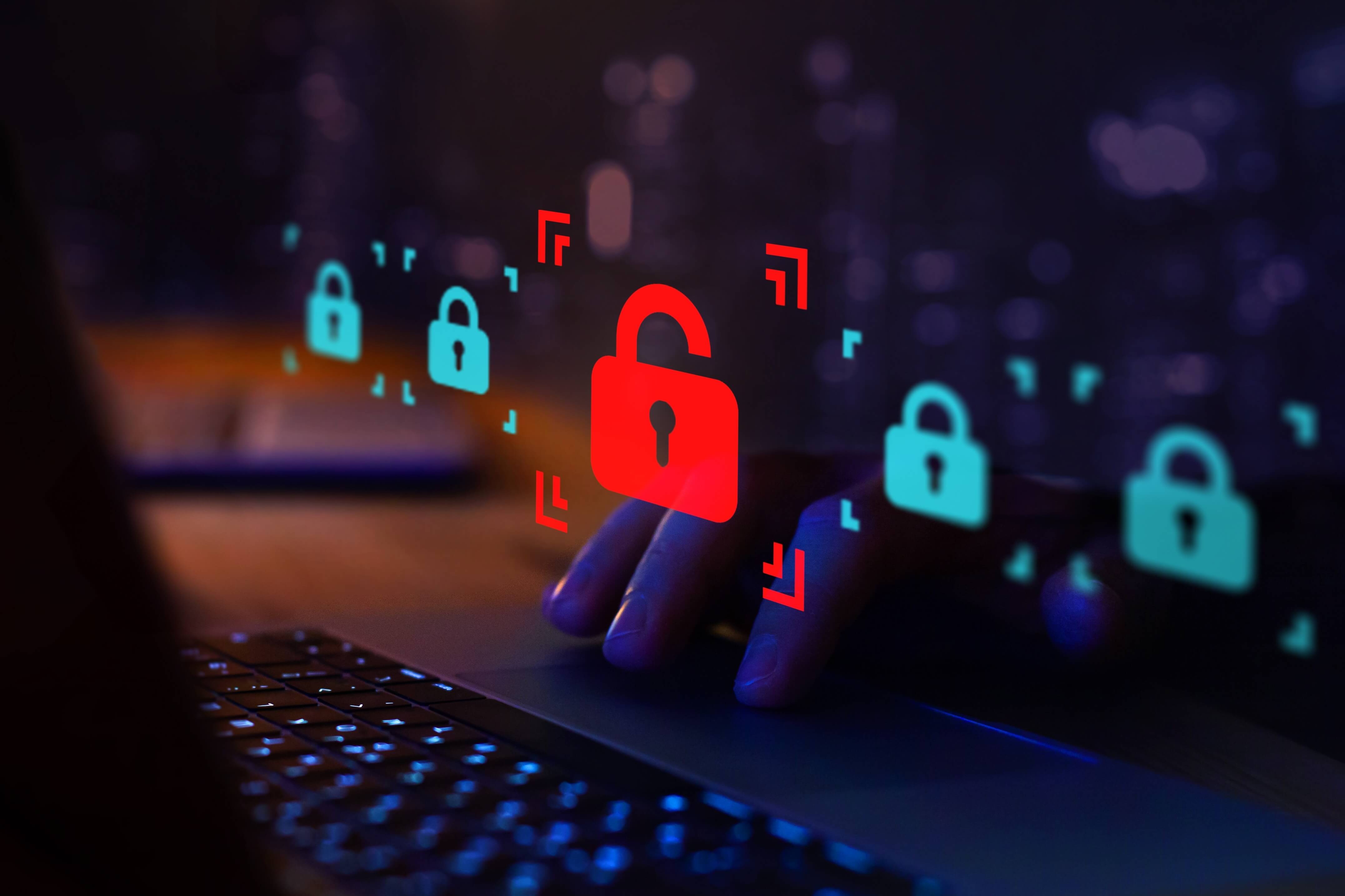Close-up of hands typing on a laptop with holographic padlock icons, highlighting a red unlocked padlock symbolising a cybersecurity breach or data vulnerability.