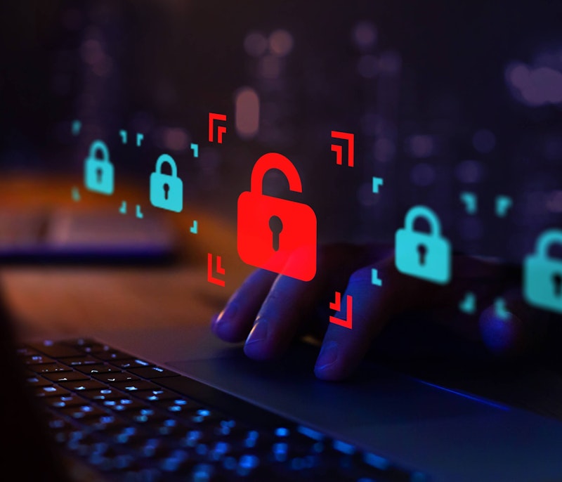 Close-up of hands typing on a laptop with holographic padlock icons, highlighting a red unlocked padlock symbolising a cybersecurity breach or data vulnerability.