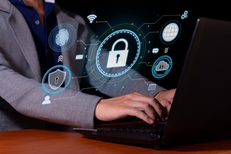 Person typing on a laptop with holographic cybersecurity icons, including a padlock, fingerprint, cloud, and shield, symbolising digital protection and secure networks.