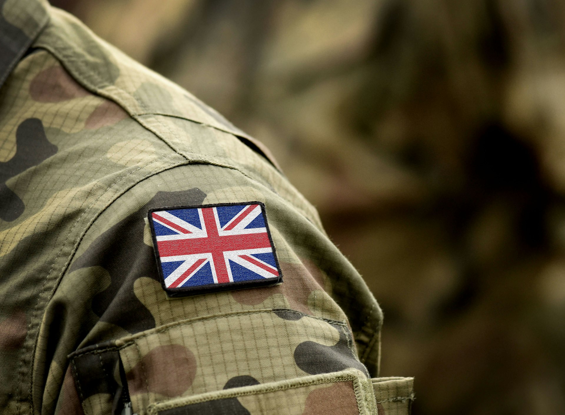 Close-up of a soldier’s camouflage uniform with a Union Jack patch on the shoulder.