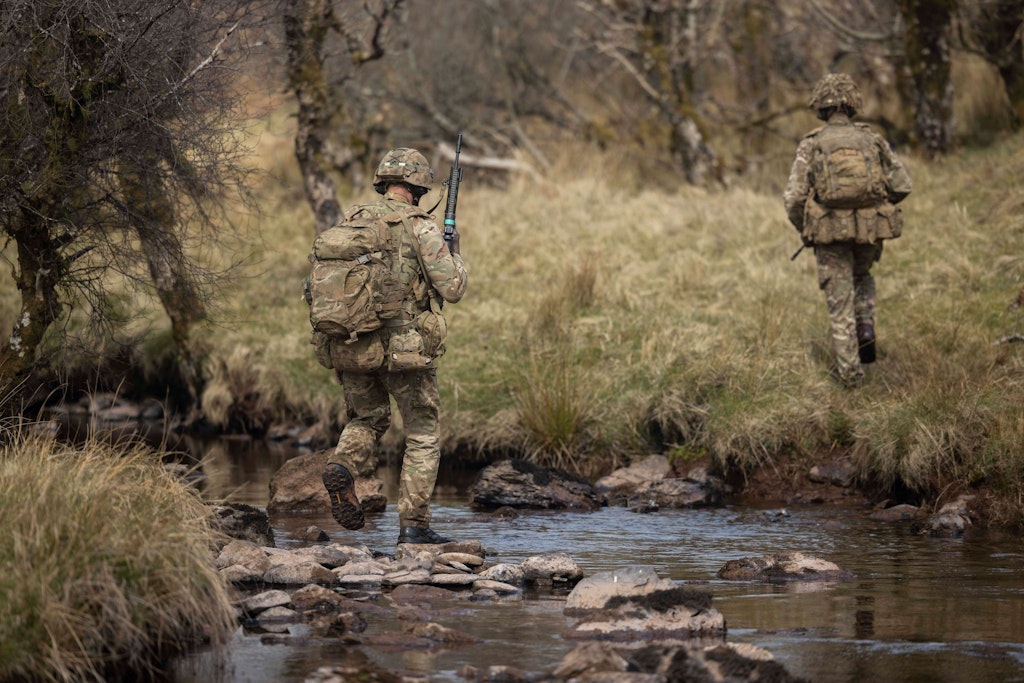Two soldiers walking through a river.
