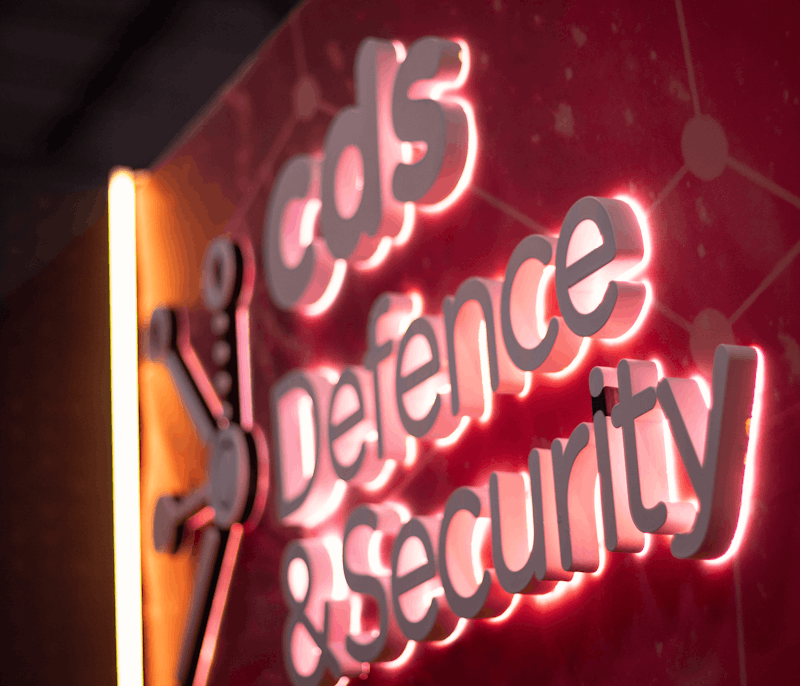Illuminated sign, reading 'CDS Defence & Security' on a red background with a connected network design.