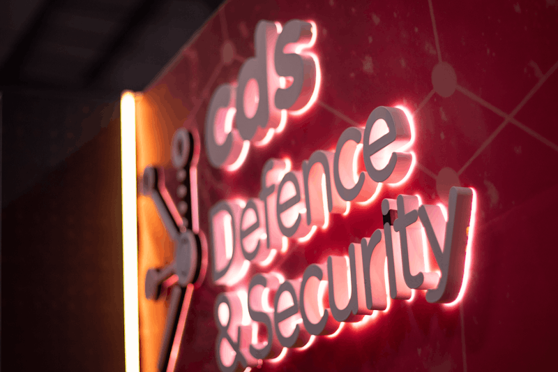 Illuminated sign, reading 'CDS Defence & Security' on a red background with a connected network design.