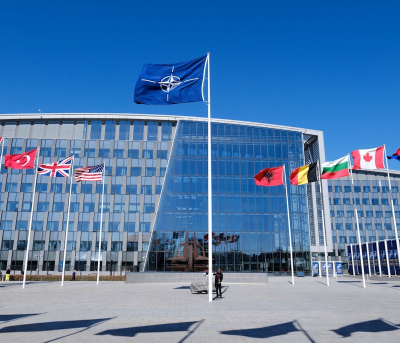 NATO headquarters building with member nation flags displayed at the entrance.