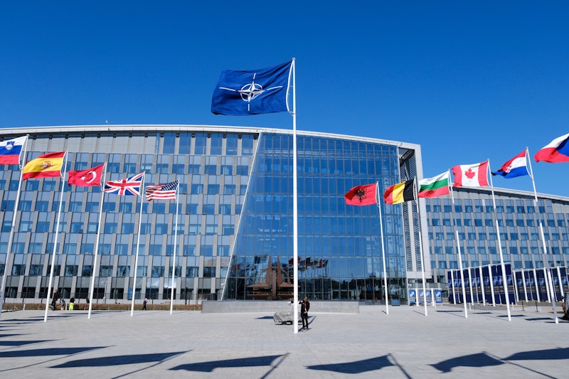 NATO headquarters building with member nation flags displayed at the entrance.