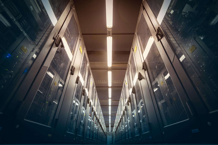 Aisle of a modern data centre with rows of server racks under bright overhead lighting.
