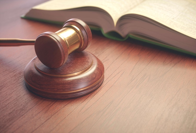 Wooden judge’s gavel resting on a block beside an open legal book, symbolising law and justice.