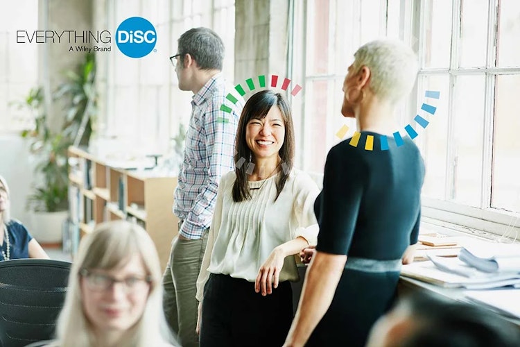 Office colleagues engaging in conversation by the window, with DiSC personality markers above them.