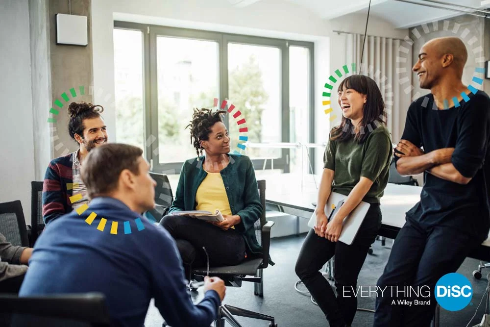 A relaxed team discussion with laughter, highlighted by colorful DiSC personality indicators.
