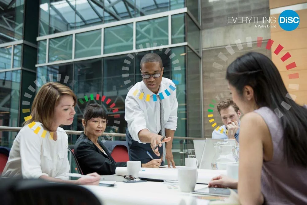Colleagues collaborating around a table, each marked with a DiSC personality style graphic.