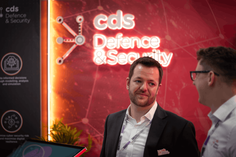 Professional networking at a defence and security event with a branded backdrop.