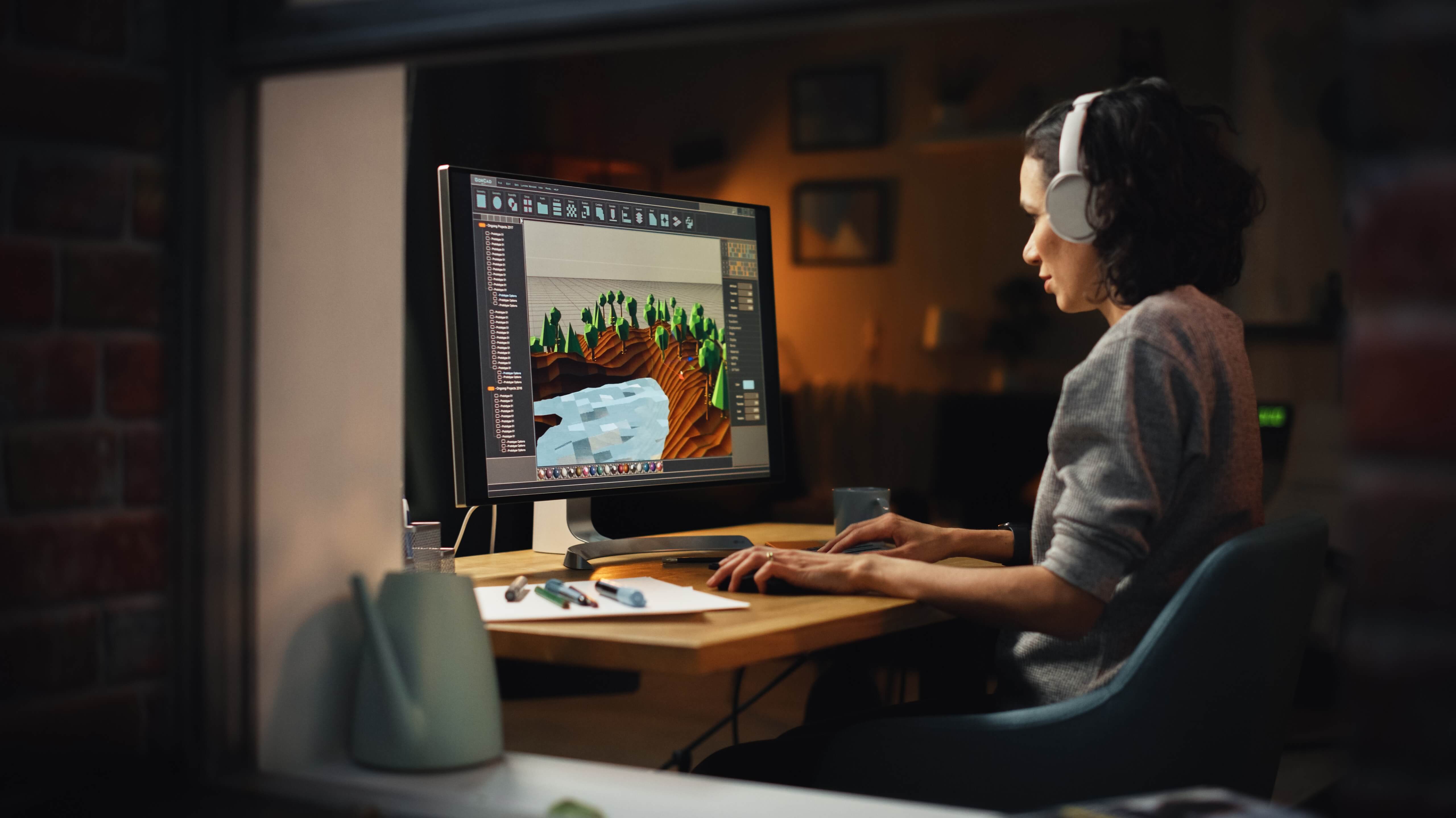 Designer creating 3D landscapes on a computer with headphones on.