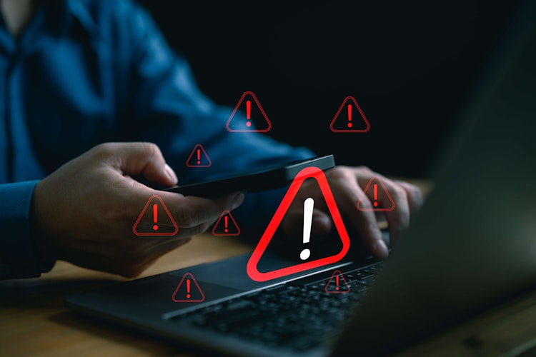 Cybersecurity concept showing multiple digital warning symbols over laptop and phone use.