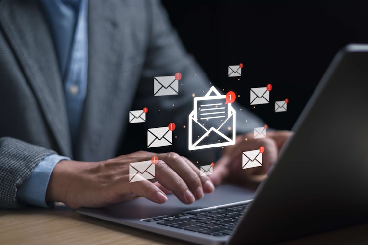 Business professional typing on a laptop with illustrated email icons and notifications.