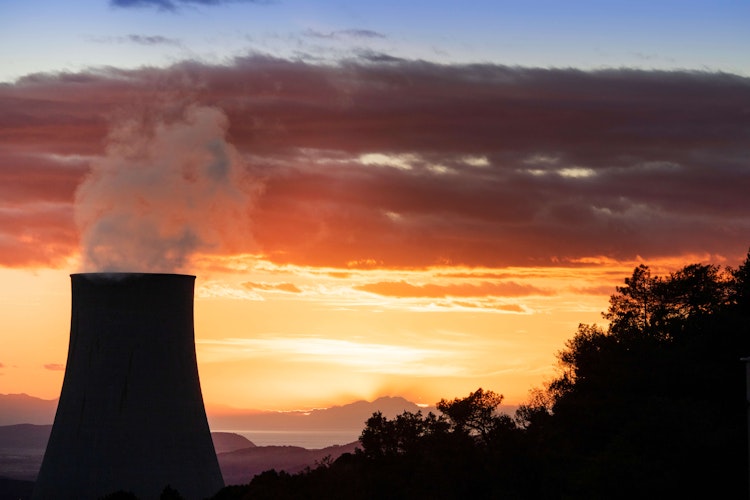 Nuclear power plant cooling tower releasing steam against a dramatic sunset sky.