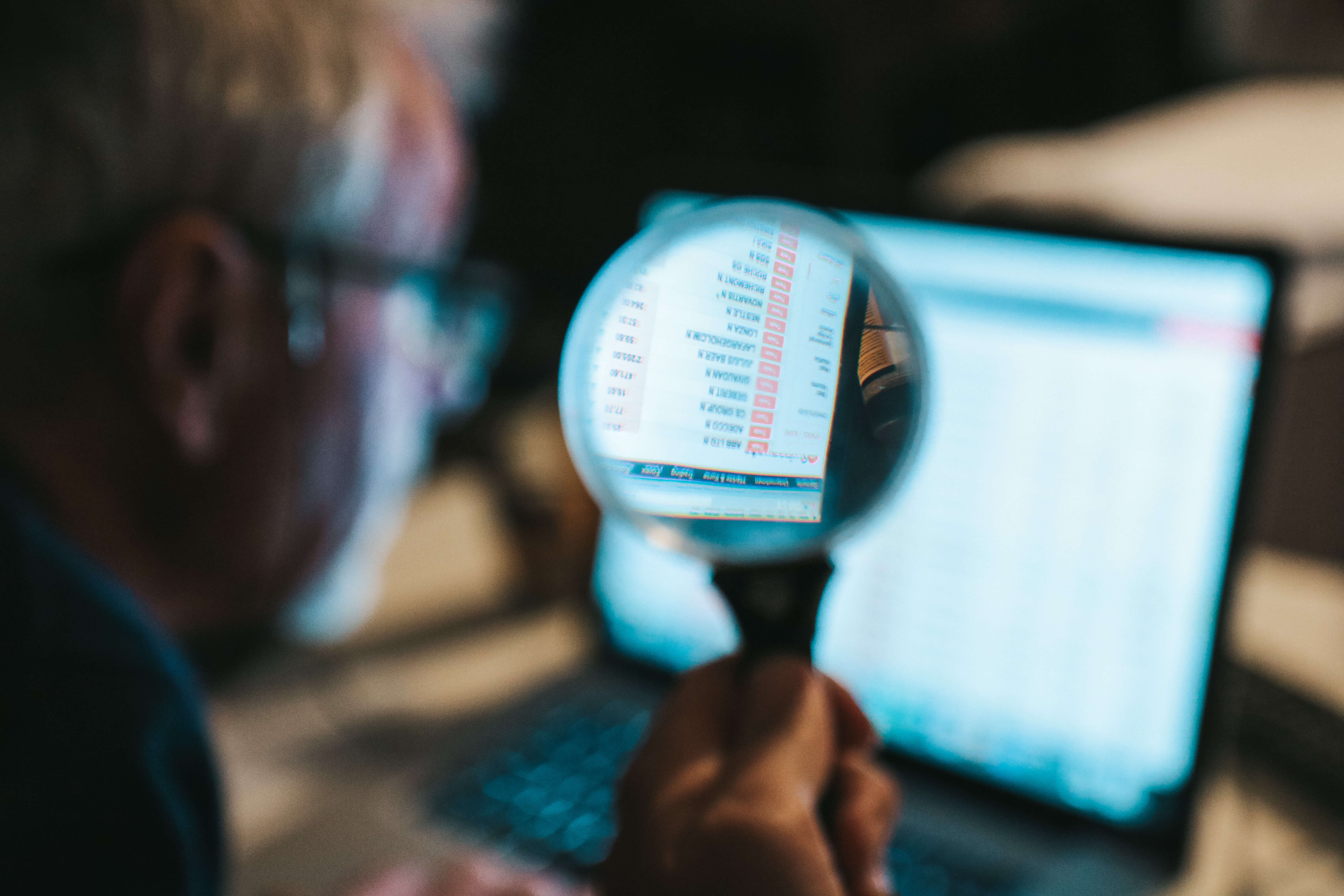 Analyst examining financial or data records on a laptop through a magnifying glass.