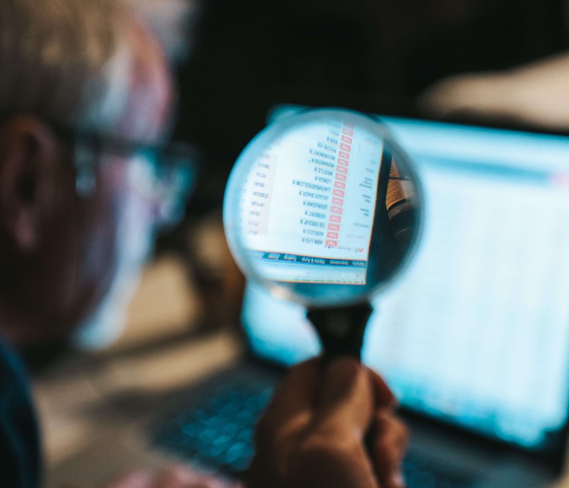 Analyst examining financial or data records on a laptop through a magnifying glass.