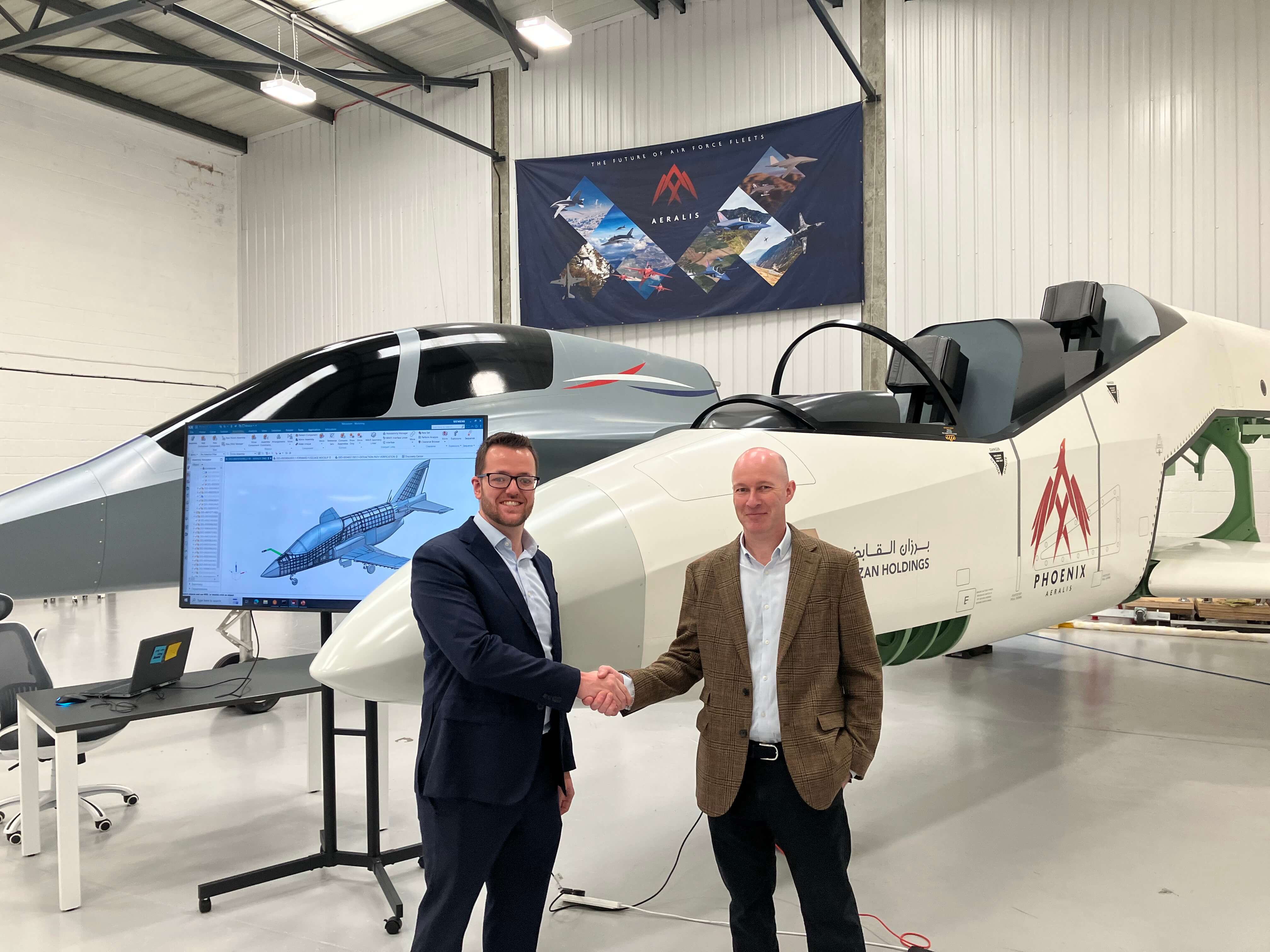 Two men shaking hands in front of a prototype aircraft inside a hangar.