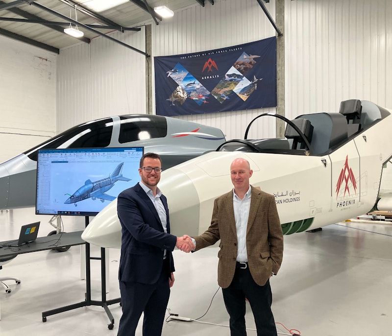 Two men shaking hands in front of a prototype aircraft inside a hangar.