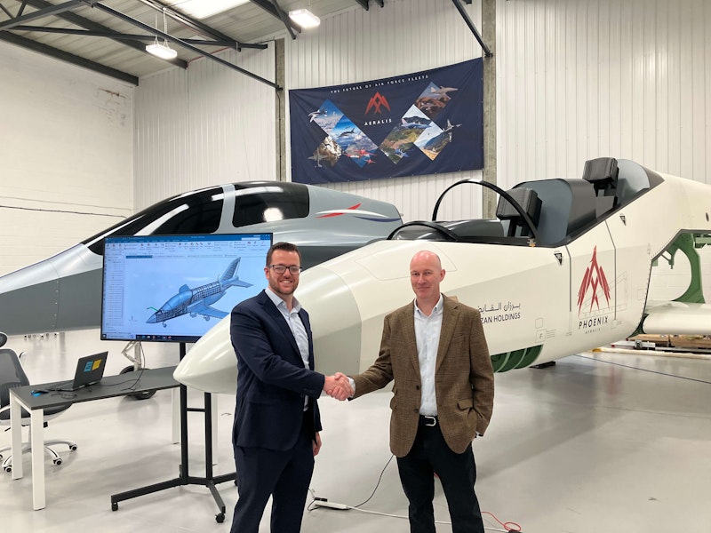 Two men shaking hands in front of a prototype aircraft inside a hangar.