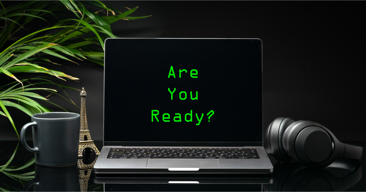 Laptop with black screen on working desk with cup and earphones on black background close up, text on screen says "are you ready?"