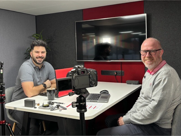 CDS DS Podcast Ep 6 Two CDS DS employees Karl Rees and Graham Hill smiling sat down in a meeting room infront of cameras, ready t orecord a podcast