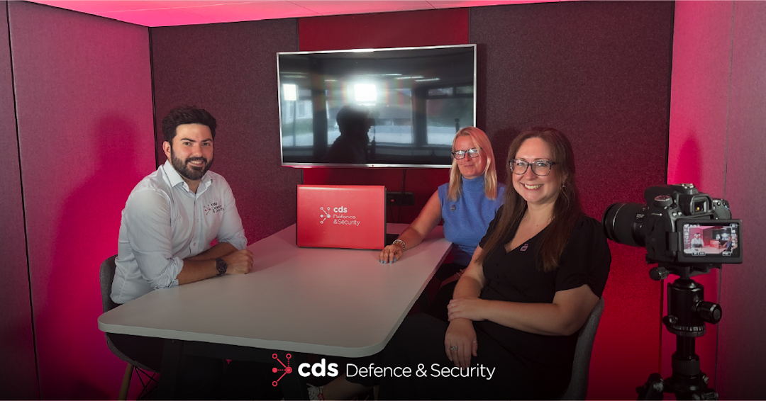 CDS DS Demystifying Cyber Podcast Episode Promotional image for the CDS Defence & Security Demystifying Cyber Podcast, showing Karl Rees seated at a table with two female podcast guests Helen Pierce and Channelle Smyth in a red-lit studio. A CDS Defence & Security branded laptop sits on the table, with a camera visible in the foreground.