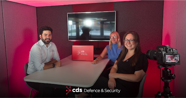 Promotional image for the CDS Defence & Security Demystifying Cyber Podcast, showing Karl Rees seated at a table with two female podcast guests Helen Pierce and Channelle Smyth in a red-lit studio. A CDS Defence & Security branded laptop sits on the table, with a camera visible in the foreground.