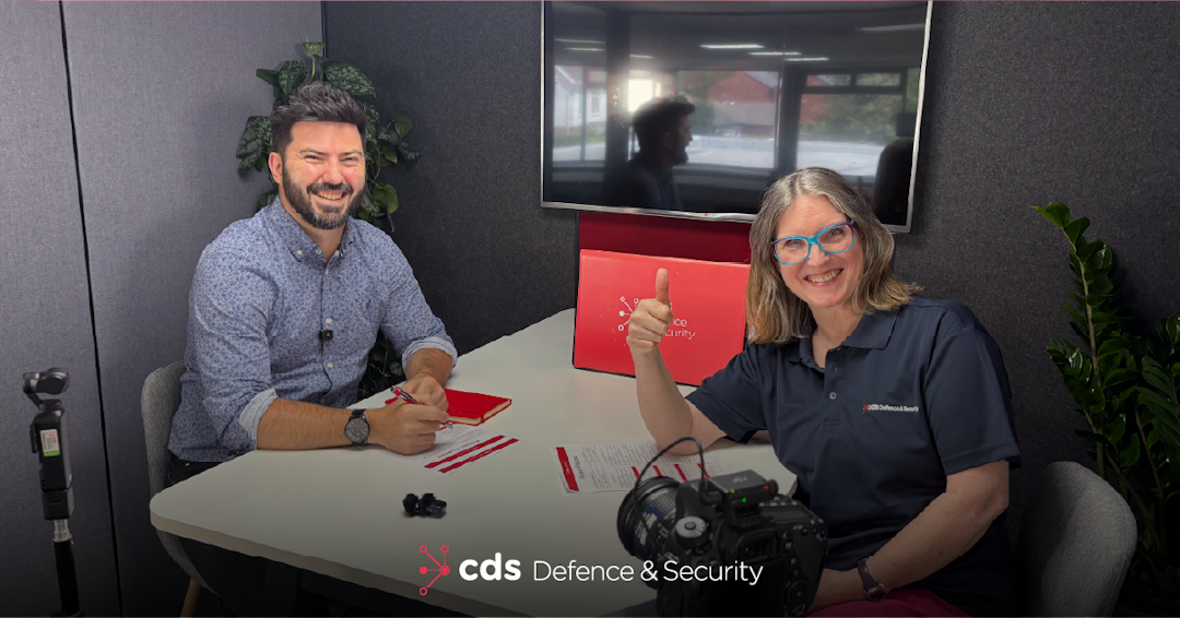 CDS DS Human Factors Podcast Episode Photo of Karl Rees and Human Factors expert Liz Hecht recording a CDS Defence & Security podcast episode about human factors. Karl sits on the left smiling towards the camera, while Liz sits on the right wearing a CDS Defence & Security polo shirt and giving a thumbs-up. They are seated around a table with recording equipment, notes and a CDS-branded laptop, with a camera visible in the foreground.