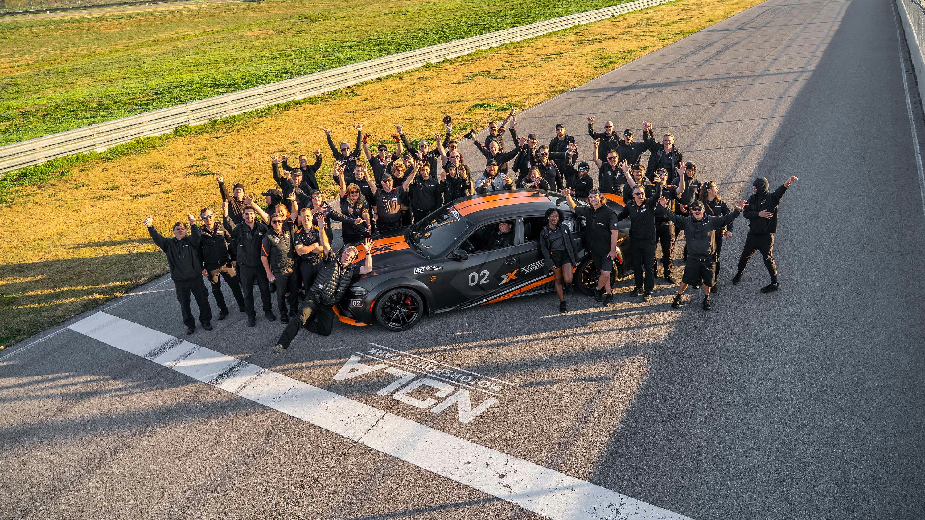 Xtreme Xperience Team The Xtreme Xperience team posing at the NOLA Motorsports Park event on the racetrack surrounding a Hellcat Charger.