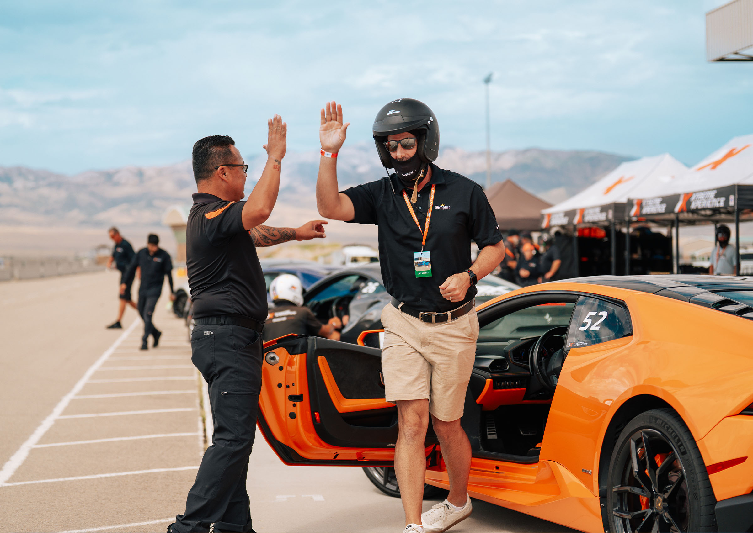 Man in all black high fiving a customer getting out of an Lamborghini Huracan in khaki shorts and a black shirt after his supercar driving experience with Xtreme Xperience at Burt Brothers Motorpark