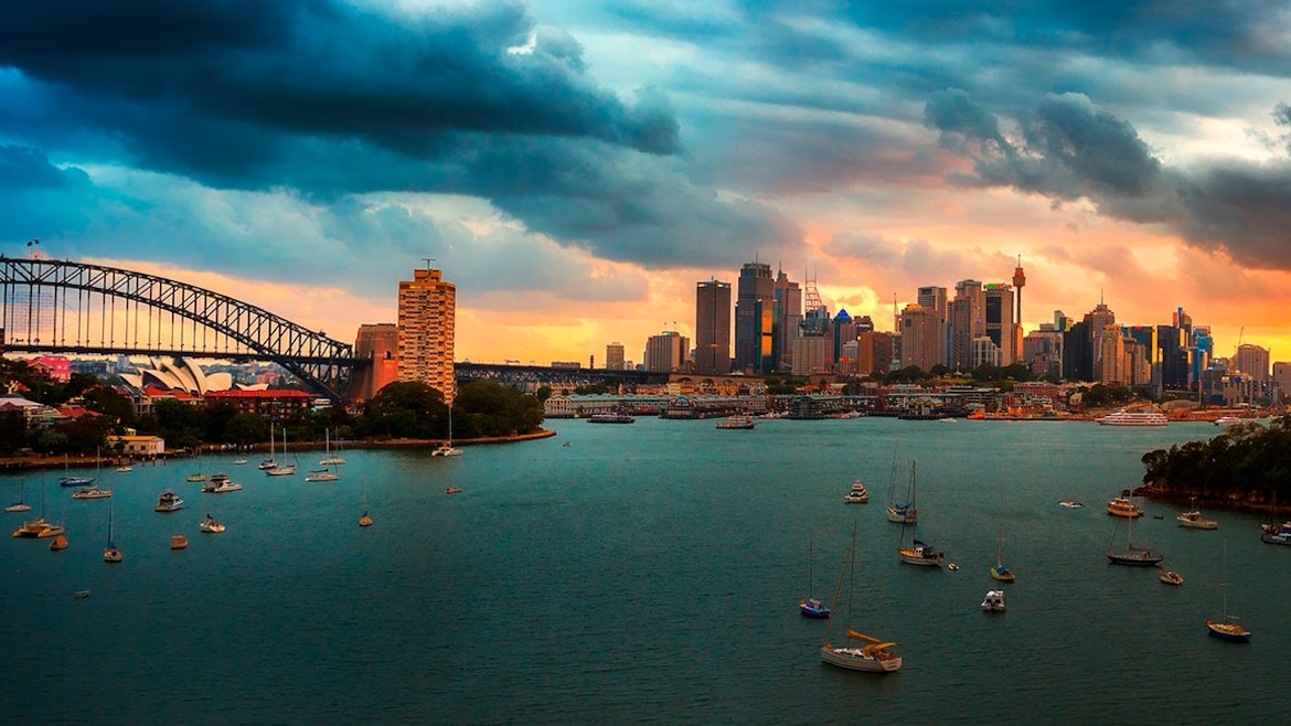 Panorama of the Sydney city skyline in the background including the Sydney Harbour Bridge and the Sydney Opera House viewed from the northern foreshore with moored boats in the foreground.
