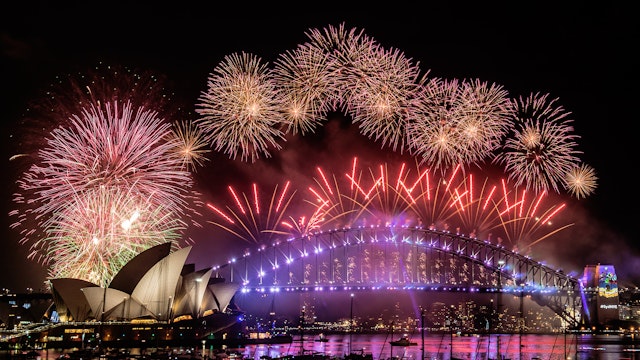 Fireworks explode from the arch of an illuminated Sydney Harbour Bridge with the harbour packed with spectator vessels.