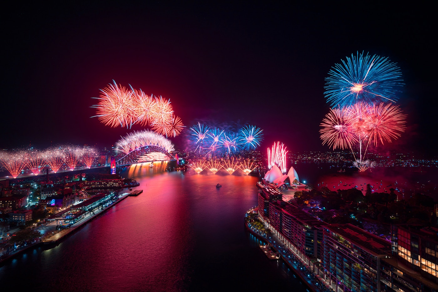 Aerial view of Sydney Harbour at night with colorful fireworks lighting up the sky above the Sydney Opera House and Harbour Bridge.