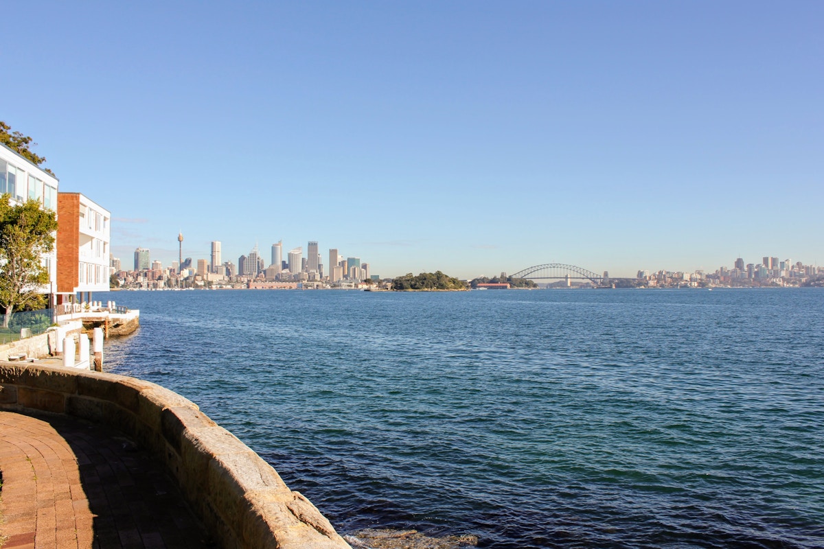 View of Sydney Harbour with city skyline, Sydney Tower, and Sydney Harbour Bridge in the distance under a clear blue sky.