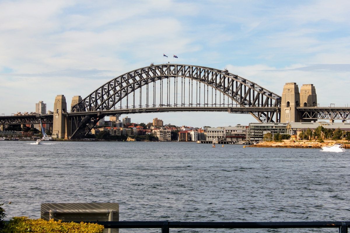 Sydney Harbour Bridge spans across the water with city buildings in the background under a partly cloudy sky.