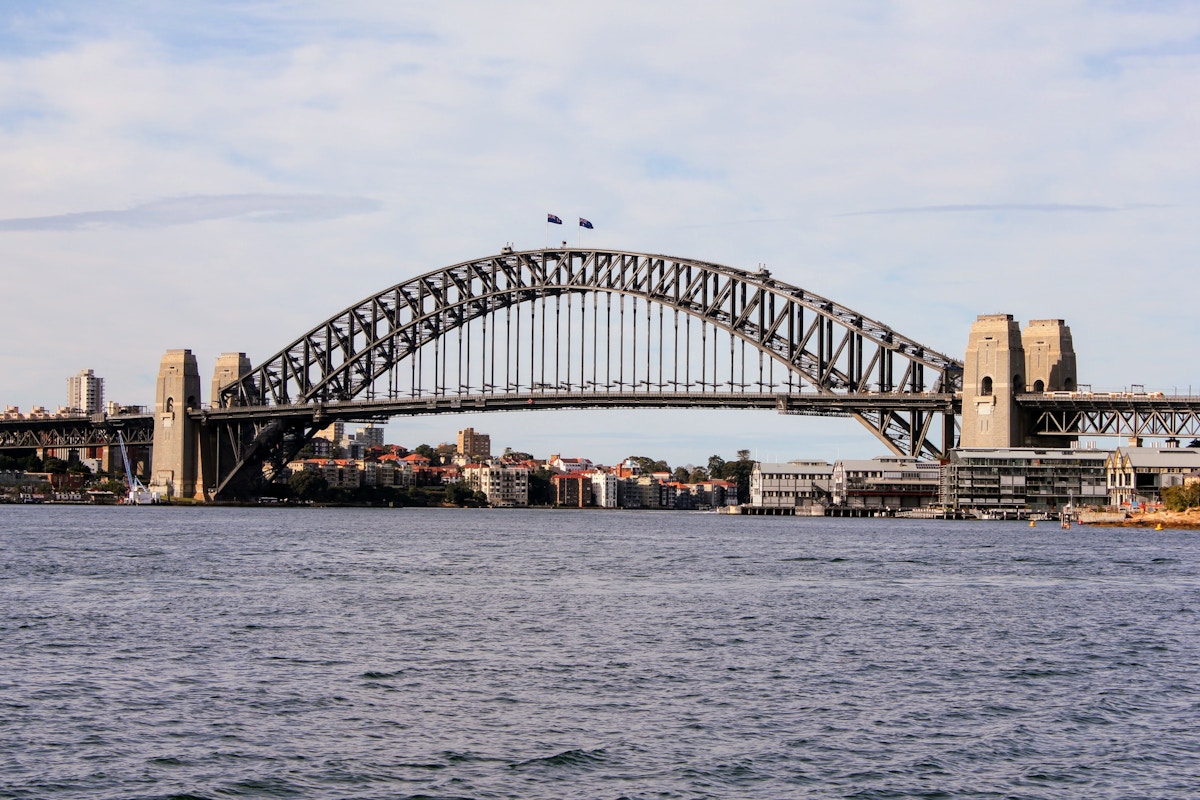 Sydney Harbour Bridge spans across the water with city buildings in the background under a partly cloudy sky.