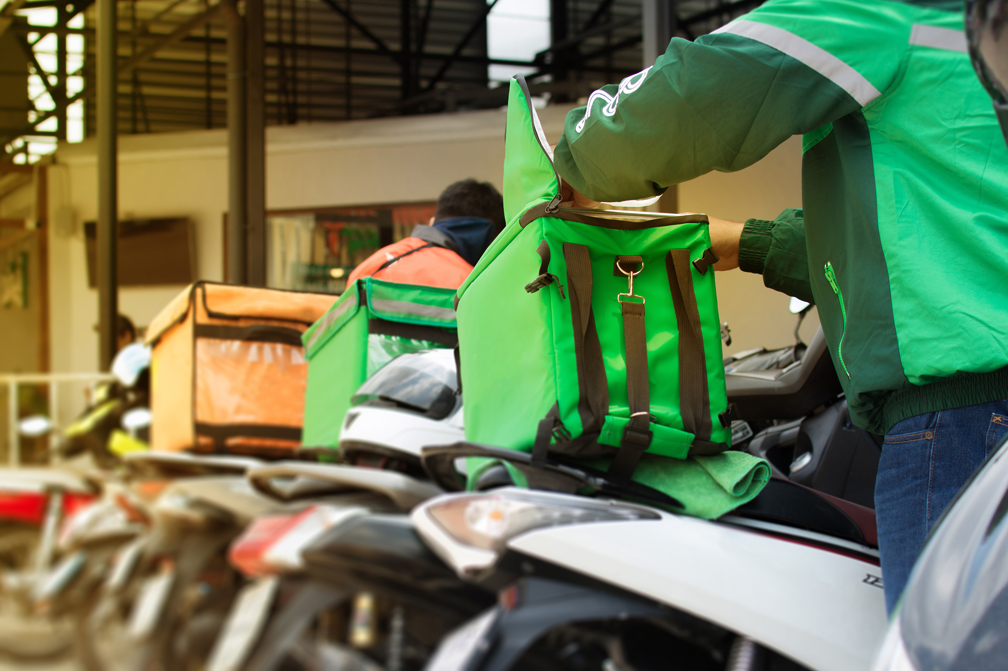 Food Delivery drivers from different couriers (food aggregators) wait with their motorcycles outside a restaurant.