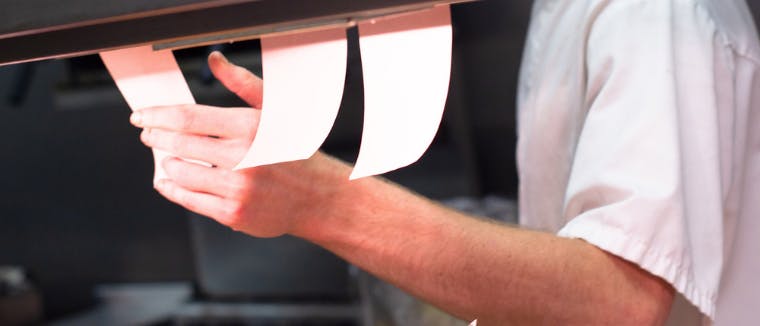 Person handling Order tickets in the kitchen. Dark kitchen or restaurant with online ordering.