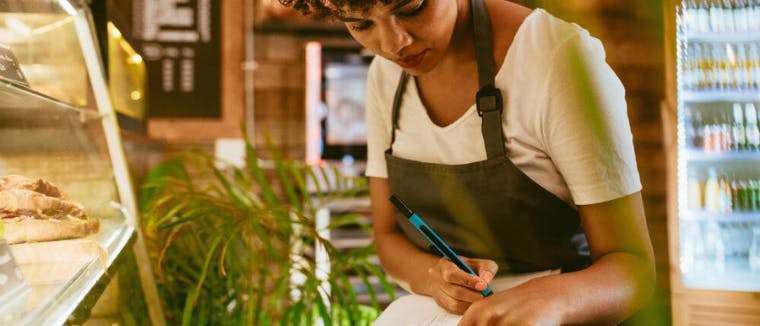 Afroamerican woman taking notes in her restaurant.