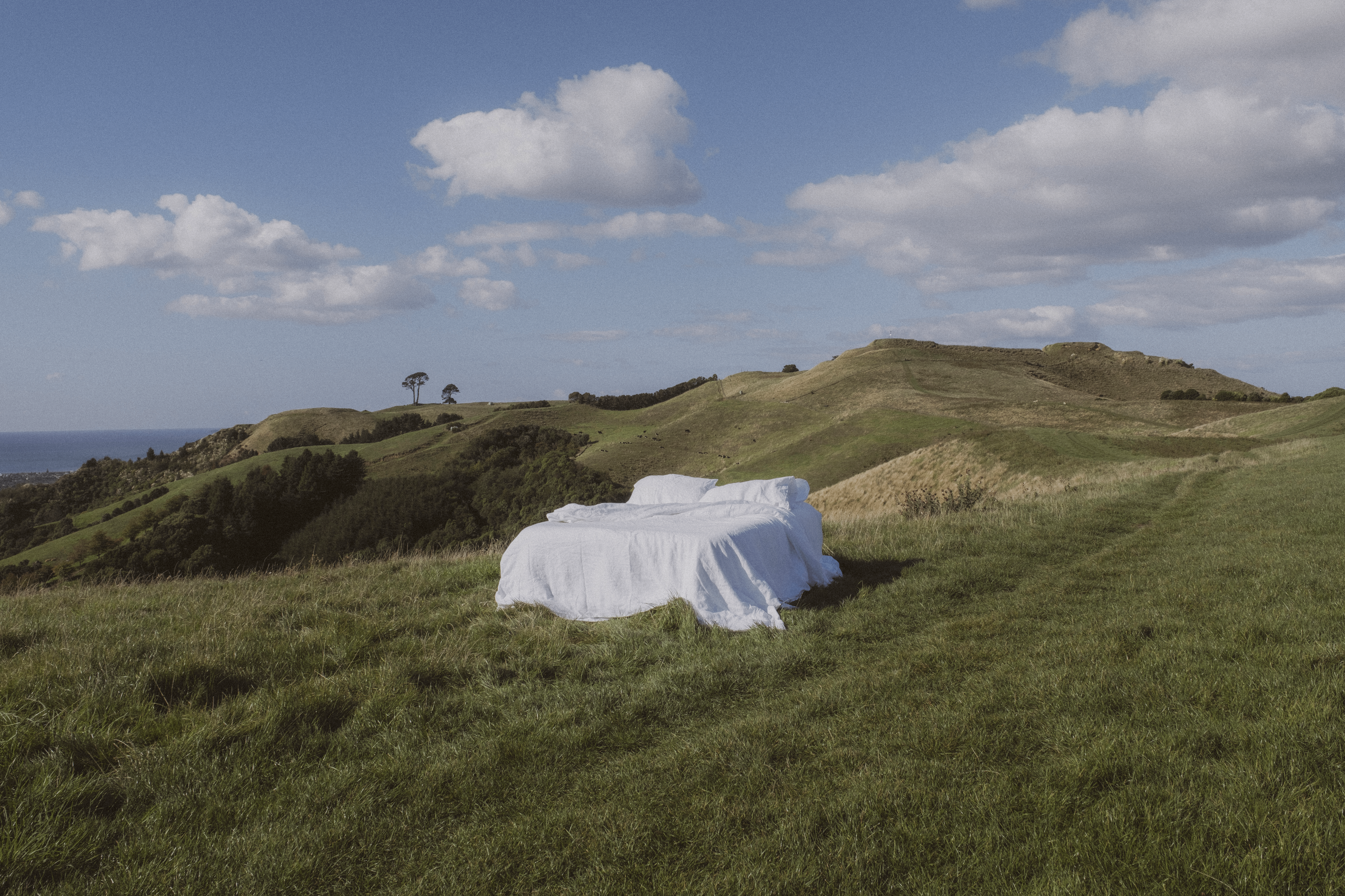 A bed with white sheets in the middle of a grassy field