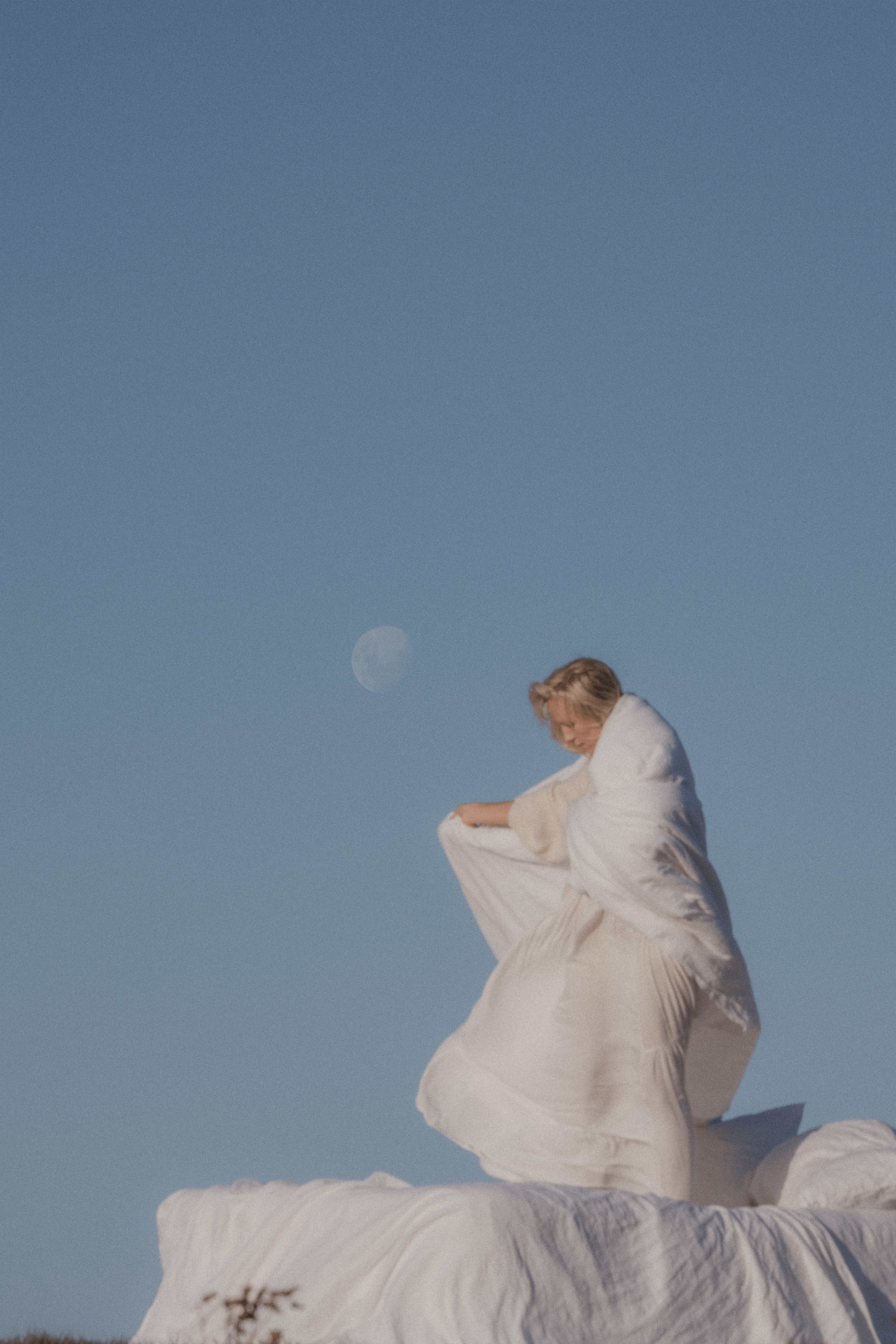 Woman standing on bed wrapped in sheets