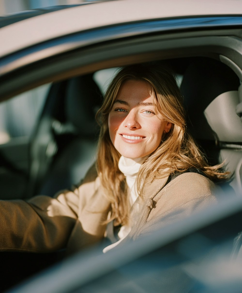 Smiling woman sitting behind the wheel of a modern car in warm natural light