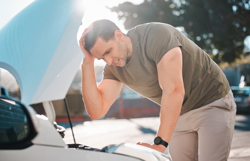 A man looking at the hood of his car