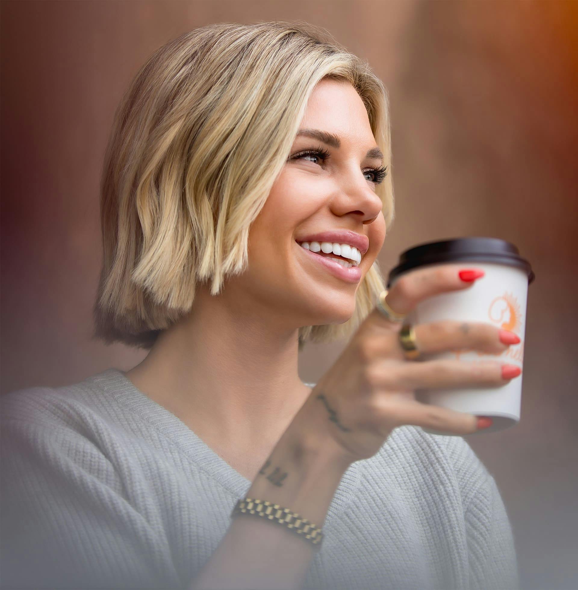 woman with short blonde hair holding a to-go coffee cup