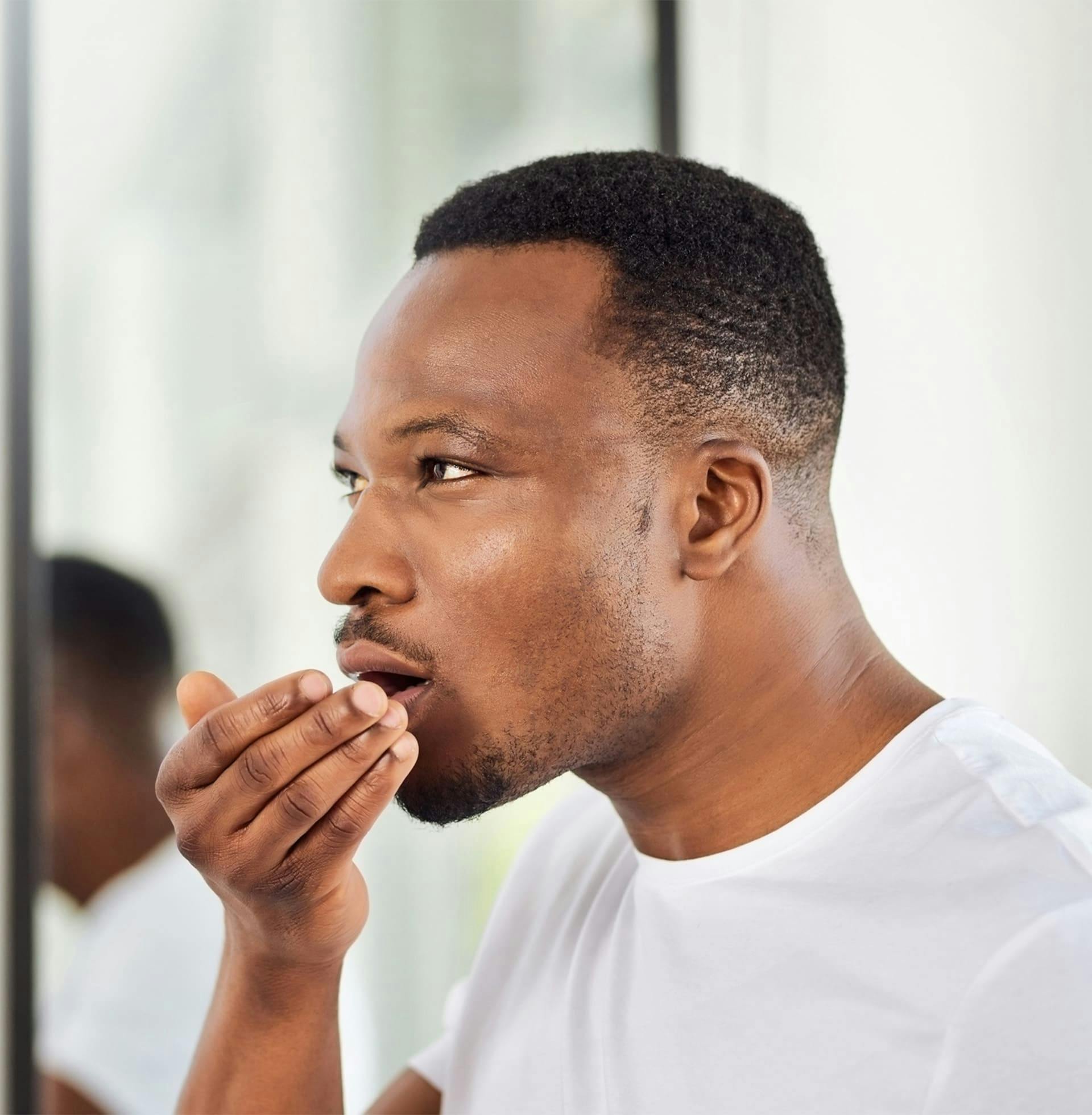 man smelling his breath in the palm of his hand