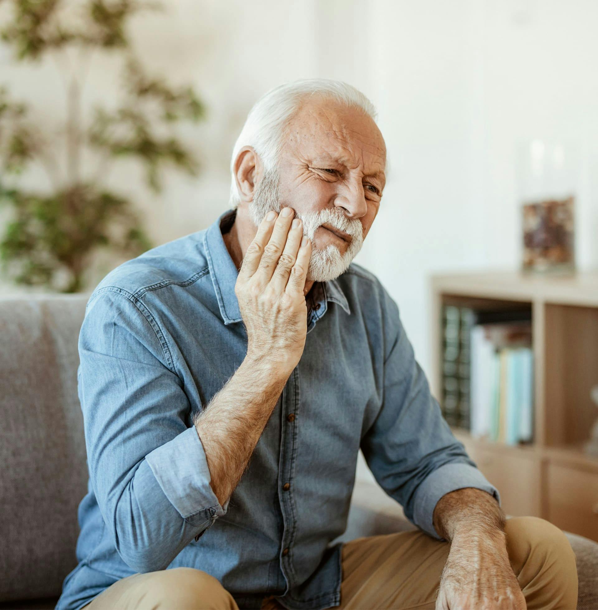 older man in pain as he touches the side of his cheek