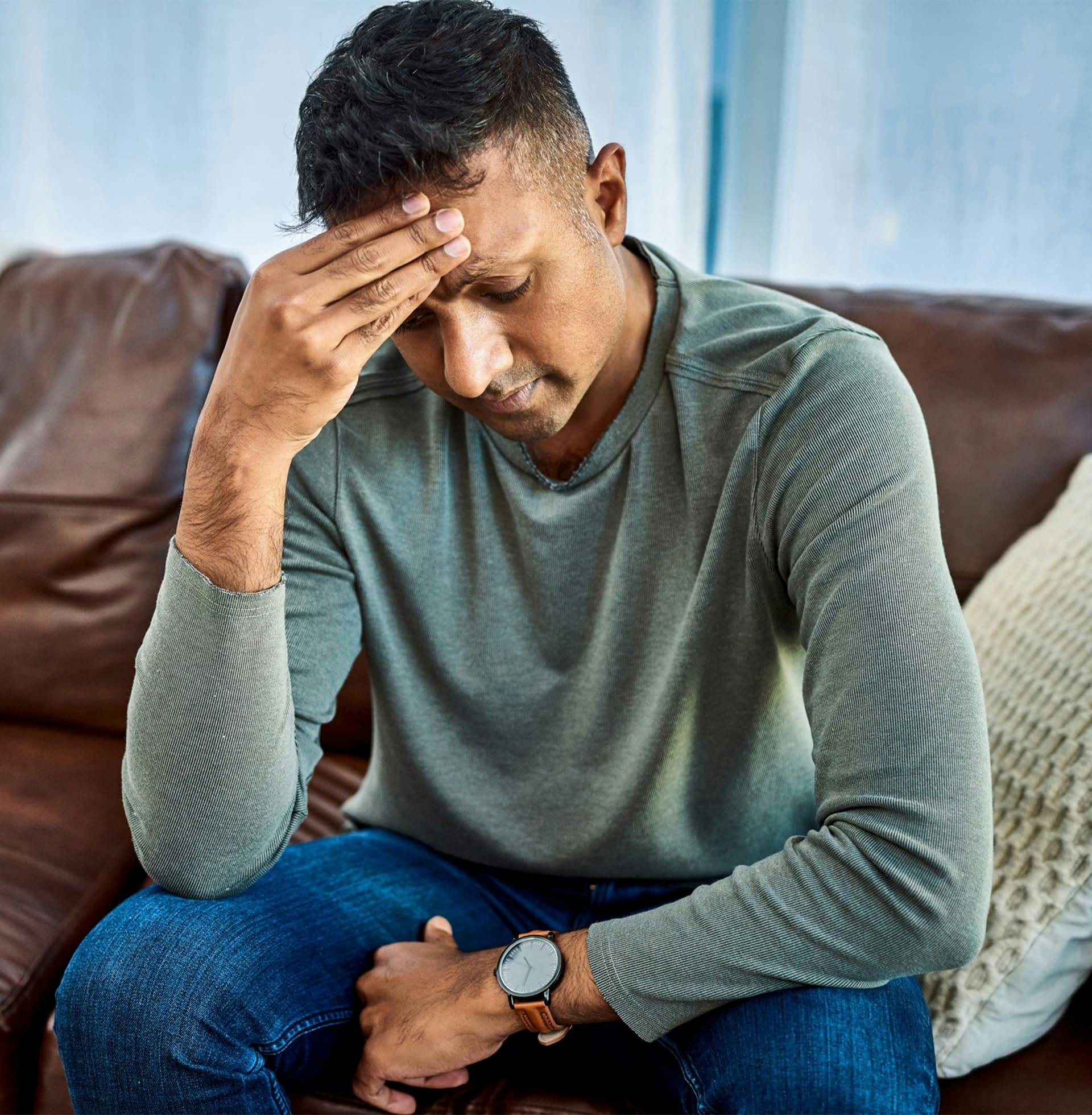 man sitting on couch with his hands on his forehead